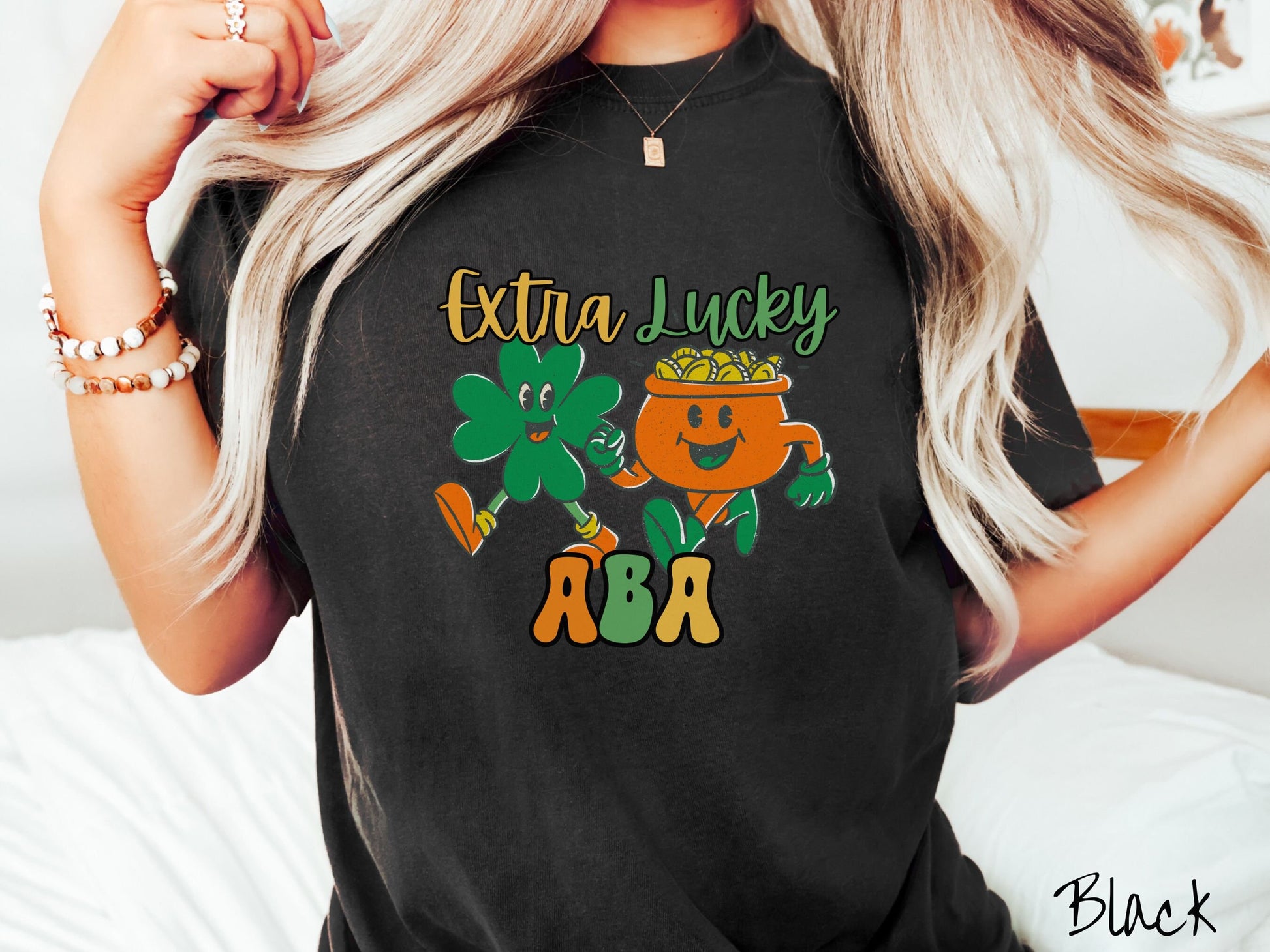 A woman wearing a vintage, black colored shirt with the text Extra Lucky ABA in yellow, orange, and green font. Between the text are a green clover and orange pot of gold smiling and walking together in step.
