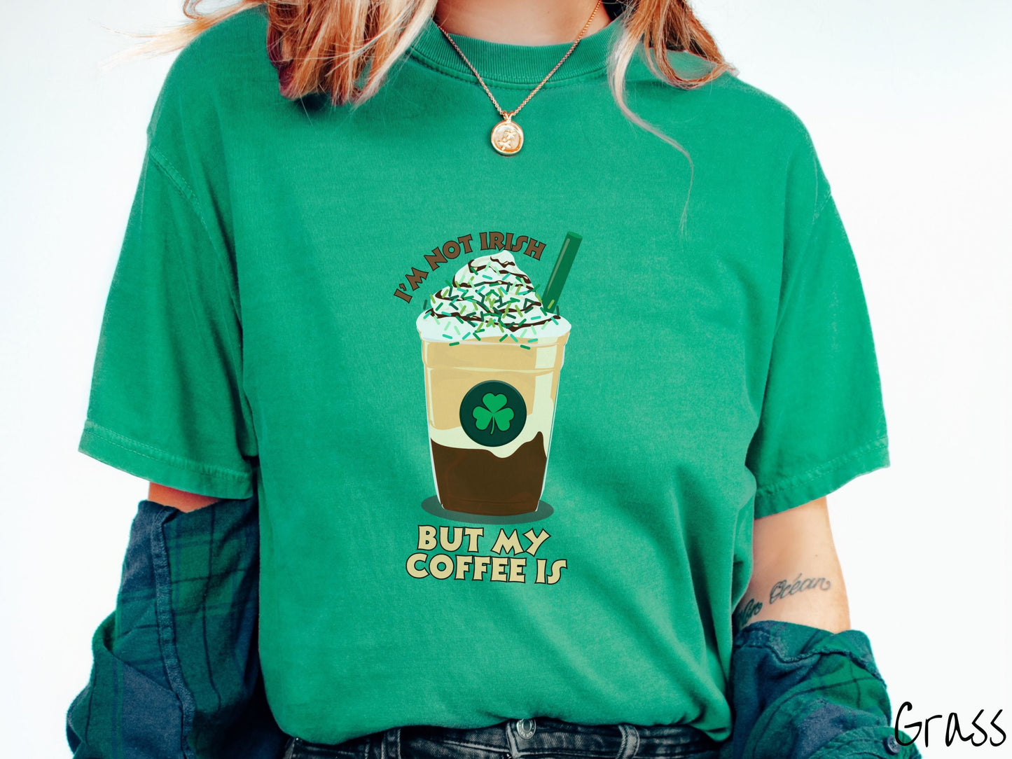 A woman wearing a vintage, grass colored shirt with the text Im not Irish but my coffee is in brown and yellow text, between the text is a green and yellow coffee cup with a green clover and  whipped cream and chocolate drizzle on top.