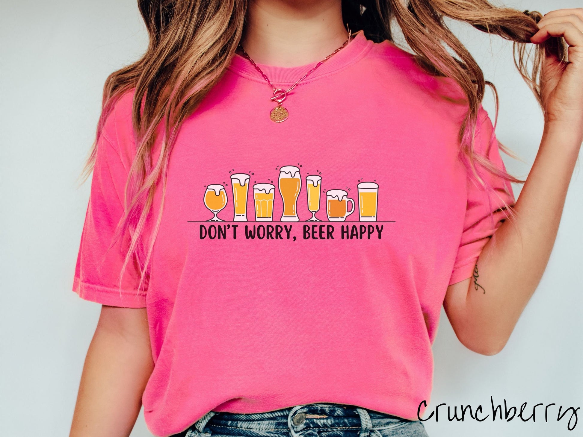 A woman wearing a vintage, crunchberry colored shirt with the text Dont Worry, Beer happy, and above this are varying sizes and shapes of beer glasses with yellow and orange ber all of them have foam coming out the tops.