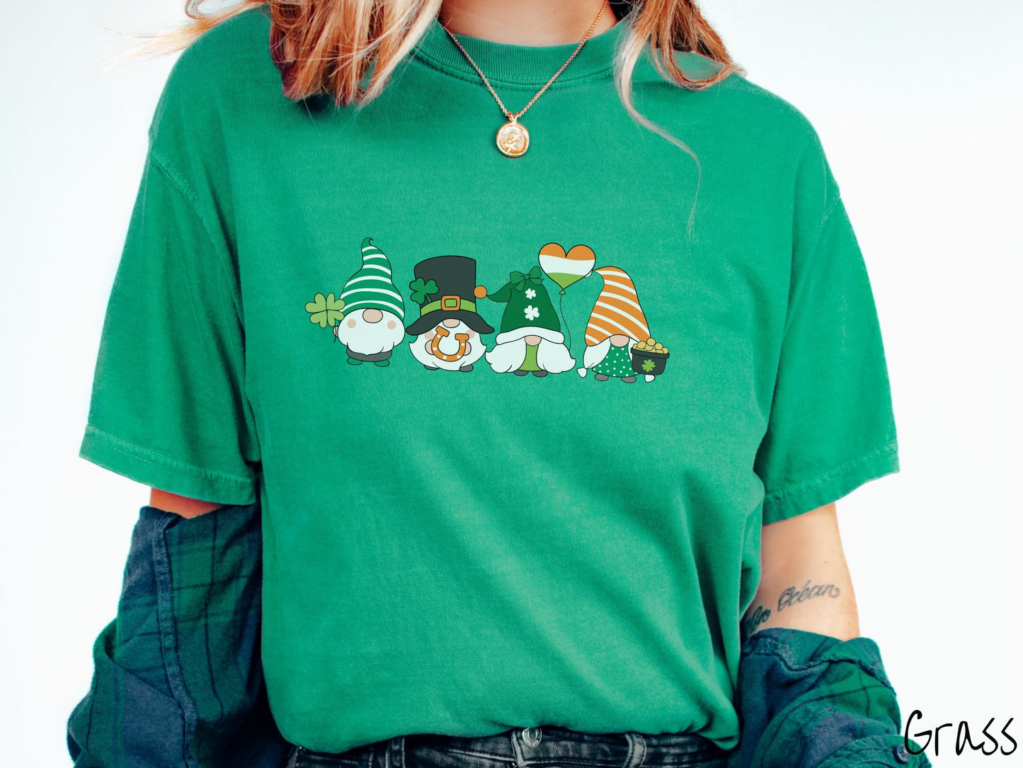 A woman wearing a vintage, grass colored shirt with four festive gnomes wearing varying green, white, and orange hats holding a green clover, an inflatable balloon, an orange horse shoe, and a pot of gold.