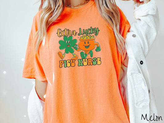 A woman wearing a vintage, melon colored shirt with the text Extra Lucky PICU Nurse  in yellow, orange, and green font. Between the text are a green clover and orange pot of gold smiling and walking together in step.