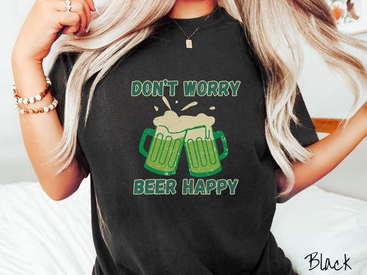 A woman wearing a vintage, black colored shirt with the green and white text Dont Worry Beer Happy, between the text are two green beer glasses with beer foaming over the tops clinking together cheering.