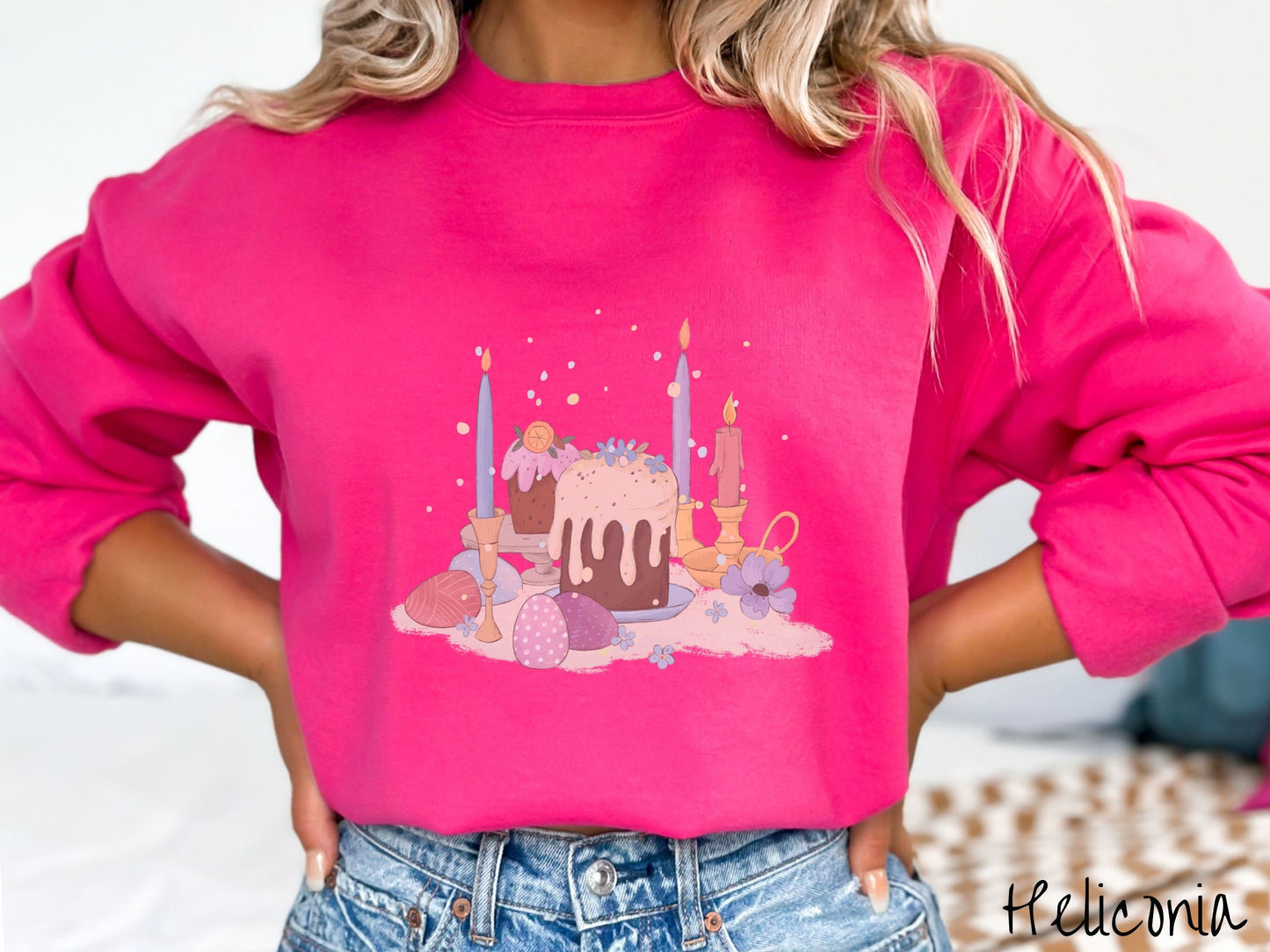 A woman wearing a cute, vintage heliconia colored sweatshirt with an assortment of colorful candles with wax running down the sides in the center, scattered around the candles are pink, purple, red, and blue colored Easter eggs.