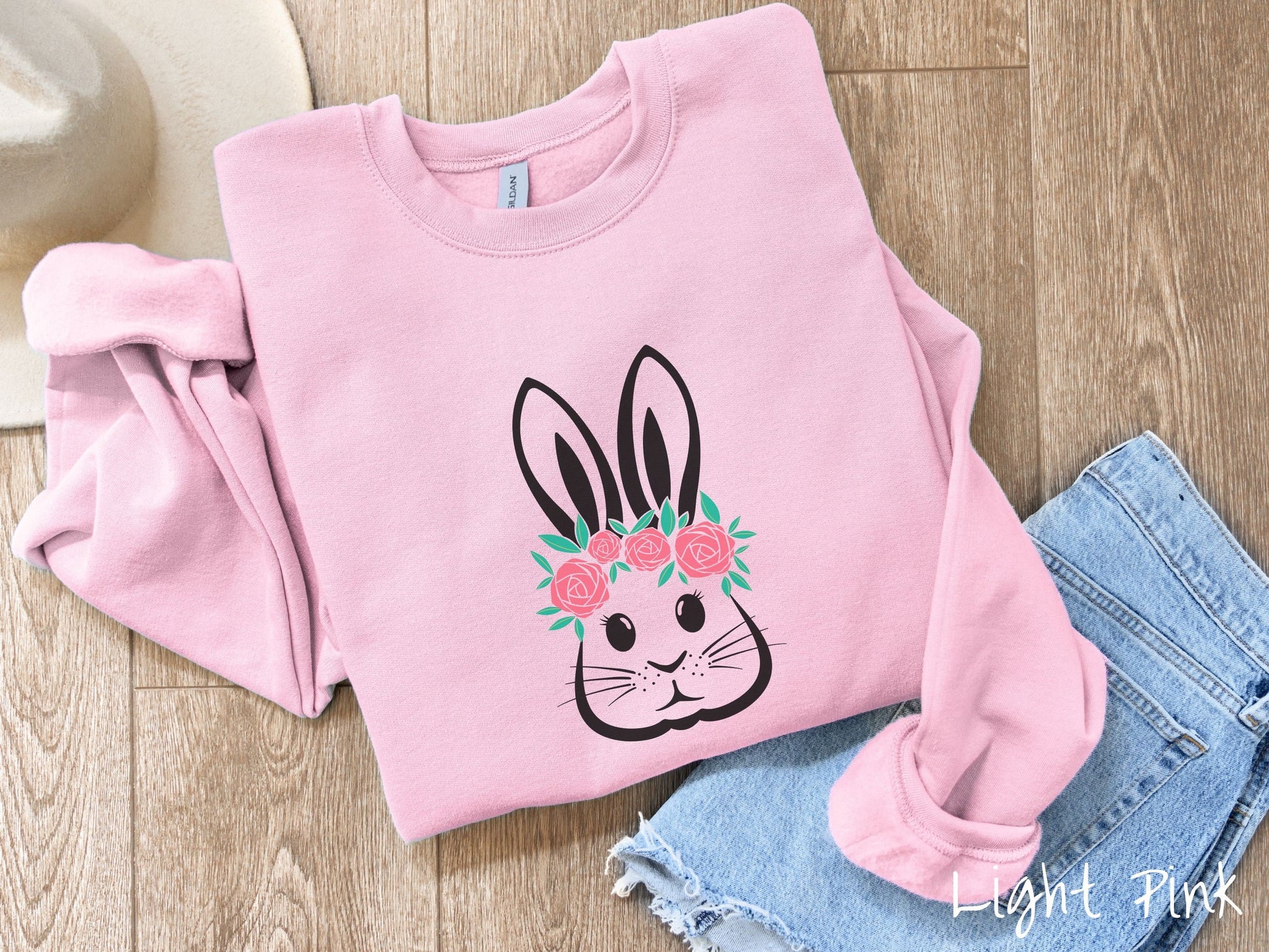 A cute, vintage light pink colored sweatshirt with a black outline of a bunny rabbit with eyelashes, whiskers, and floppy ears that has a pink flowered headband resting below its large ears.