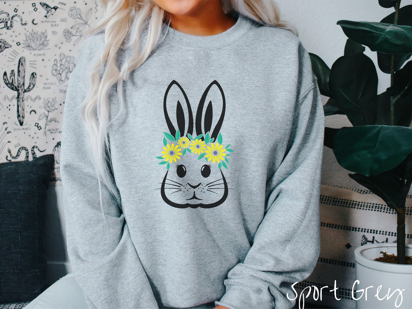 A woman wearing a cute, vintage sport grey colored sweatshirt with a black outline of a bunny rabbit with eyelashes and whiskers that has a yellow and purple flower headband resting below its large ears.