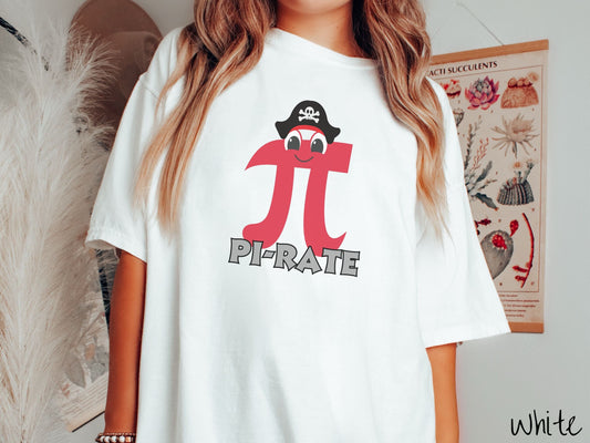 A woman wearing a cute, vintage white colored comfort colors shirt with the text PI-RATE  in gray font, above this is a red math pi symbol with eyes and a smiling face wearing a black pirate’s hat with white skull and bones on the front.