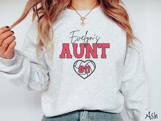 A woman wearing a cute ash colored sweatshirt with black and red text saying Evelyns Aunt. Below is a black, heart-shaped volleyball outline with #11 in red font written across it.