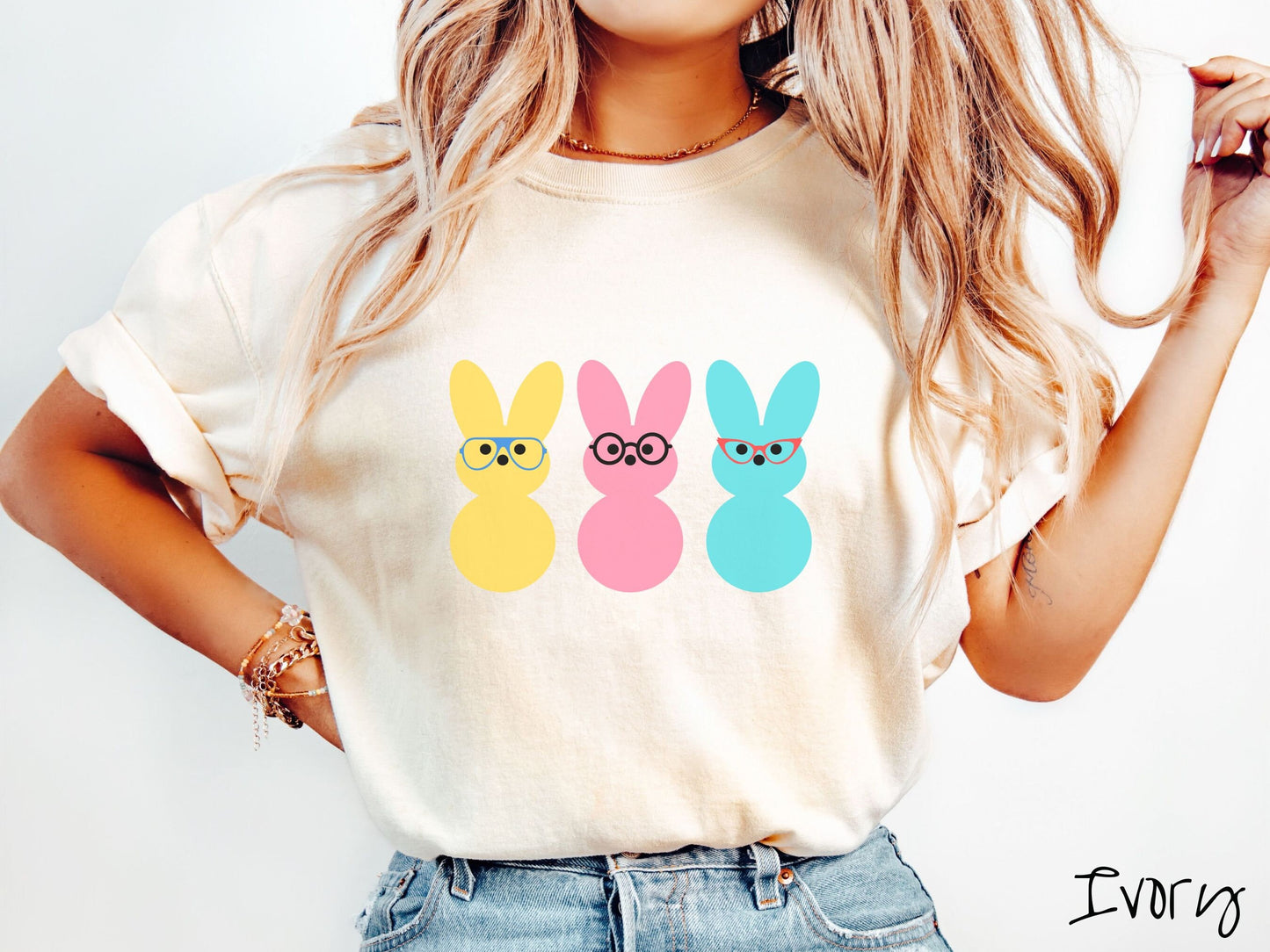 A woman wearing a cute, vintage ivory colored shirt with three peep-like rabbits on the front. One is yellow and wearing blue glasses, the middle is pink with black glasses, and the one on the right is light blue with red glasses.