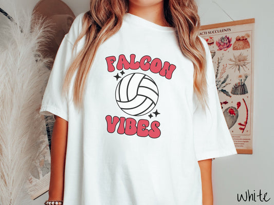 A woman wearing a cute white colored t-shirt with red text saying Falcon Vibes. There is a white volleyball with black twinkling stars around it between the text.