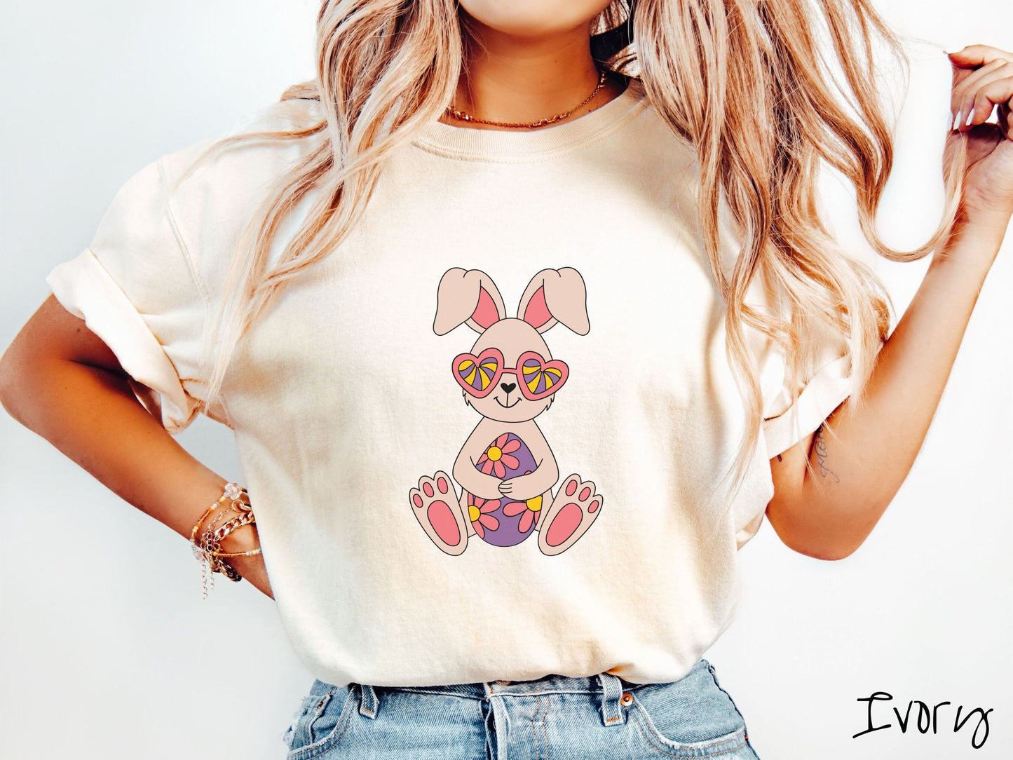 A woman wearing a cute, vintage ivory colored shirt with a smiling ivory and pink colored rabbit holding a large purple Easter egg with pink flowers. The rabbit is wearing heart-shaped pink glasses and has a heart-shaped nose.