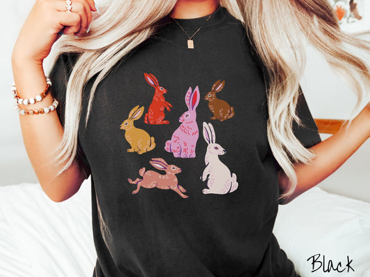 A woman wearing a cute, vintage black colored shirt with six colored bunny rabbits in different stances and postures. One is red, another brown, yellow, pink, light brown, and white.