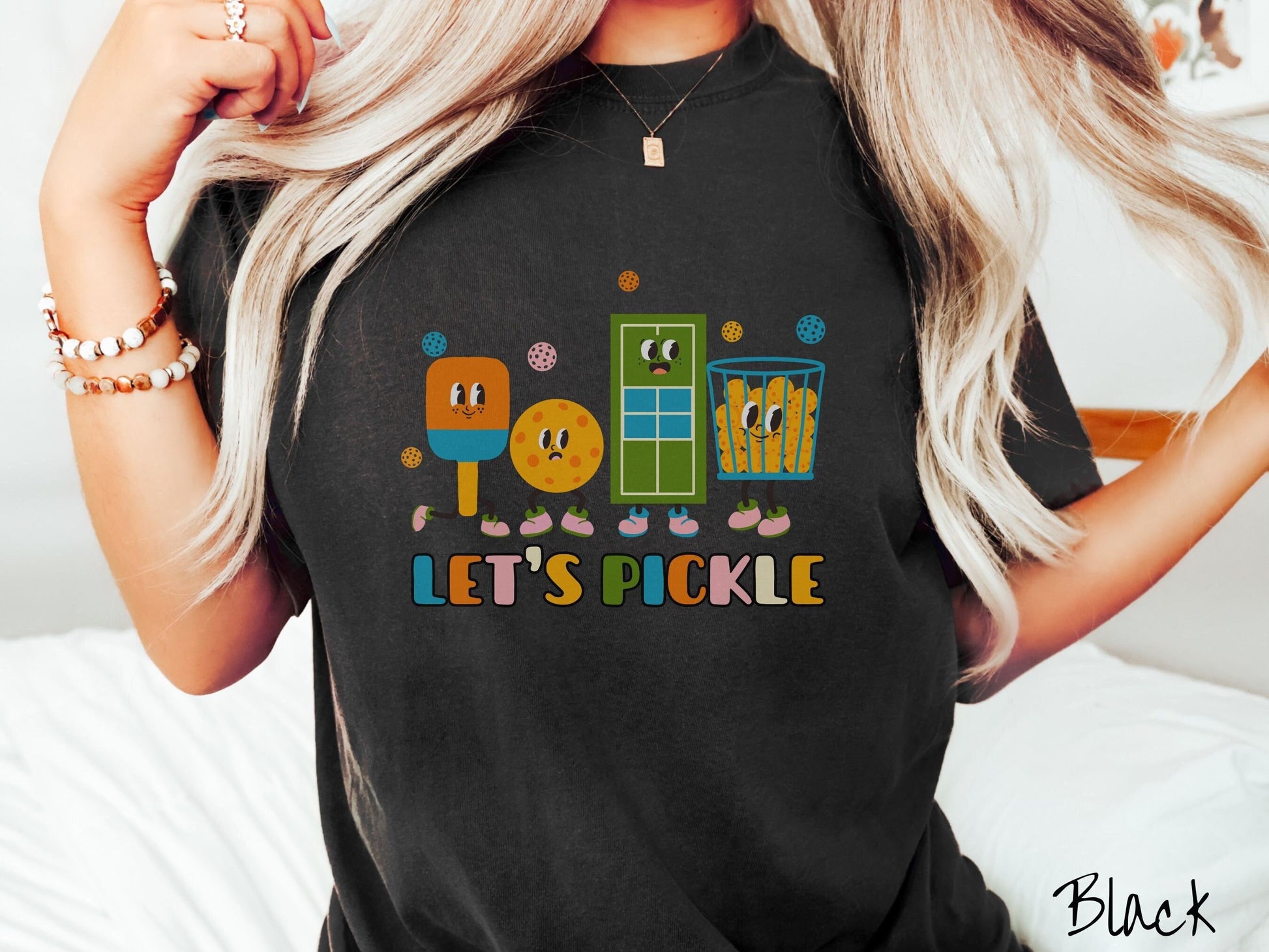 A woman wearing a cute black colored shirt with the text Let&#39;s Pickle along the bottom, and above the text are a popsicle, cookie, popcorn, and pickle balls.