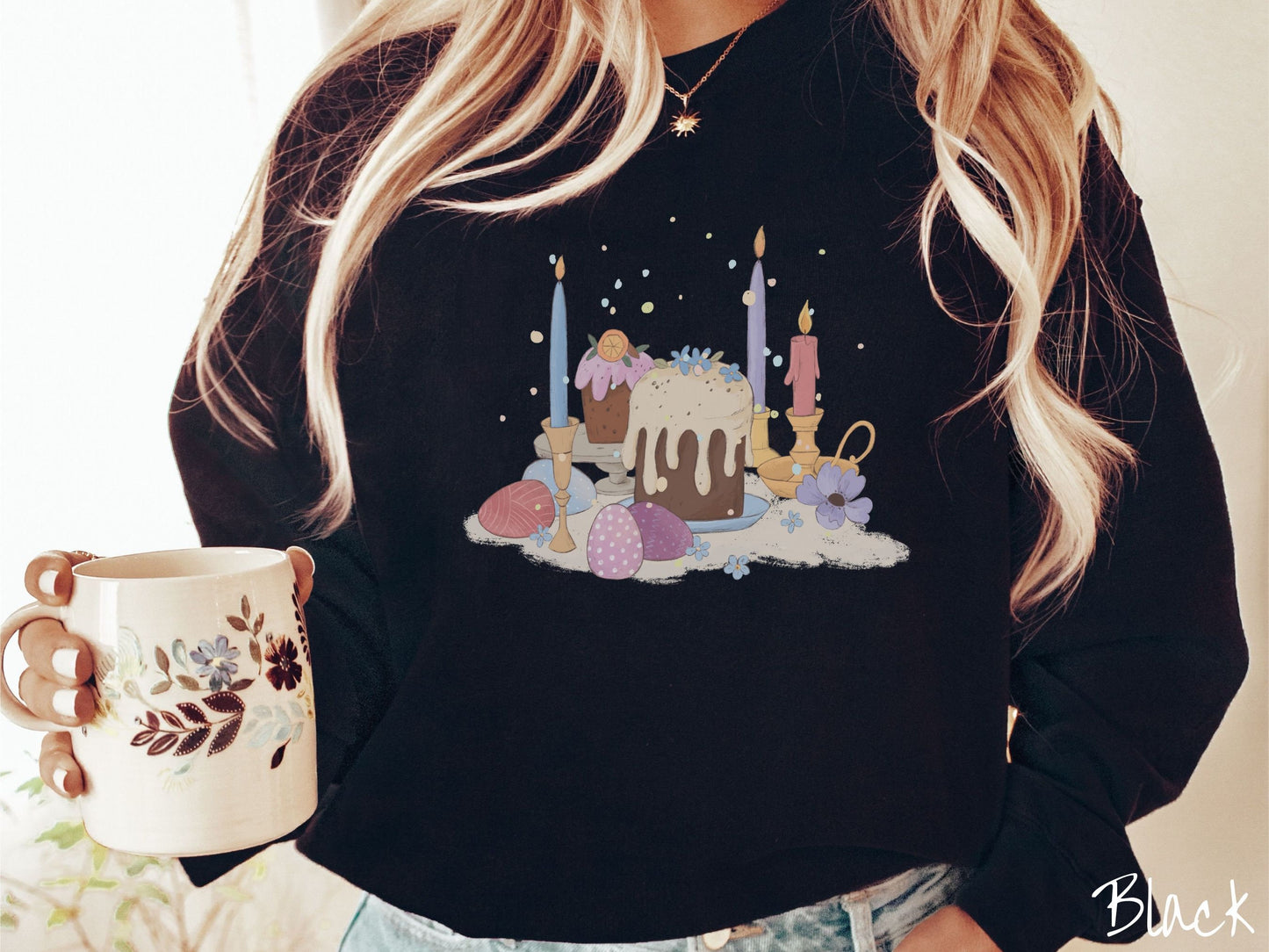 A woman wearing a cute, vintage black colored sweatshirt with an assortment of colorful candles with wax running down the sides in the center, scattered around the candles are pink, purple, red, and blue colored Easter eggs.