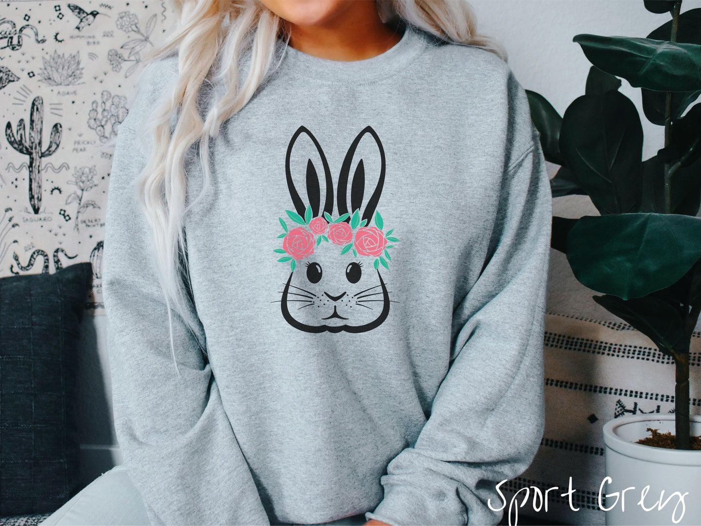 A woman wearing a cute, vintage sport grey colored sweatshirt with a black outline of a bunny rabbit with eyelashes, whiskers, and floppy ears that has a pink flowered headband resting below its large ears.