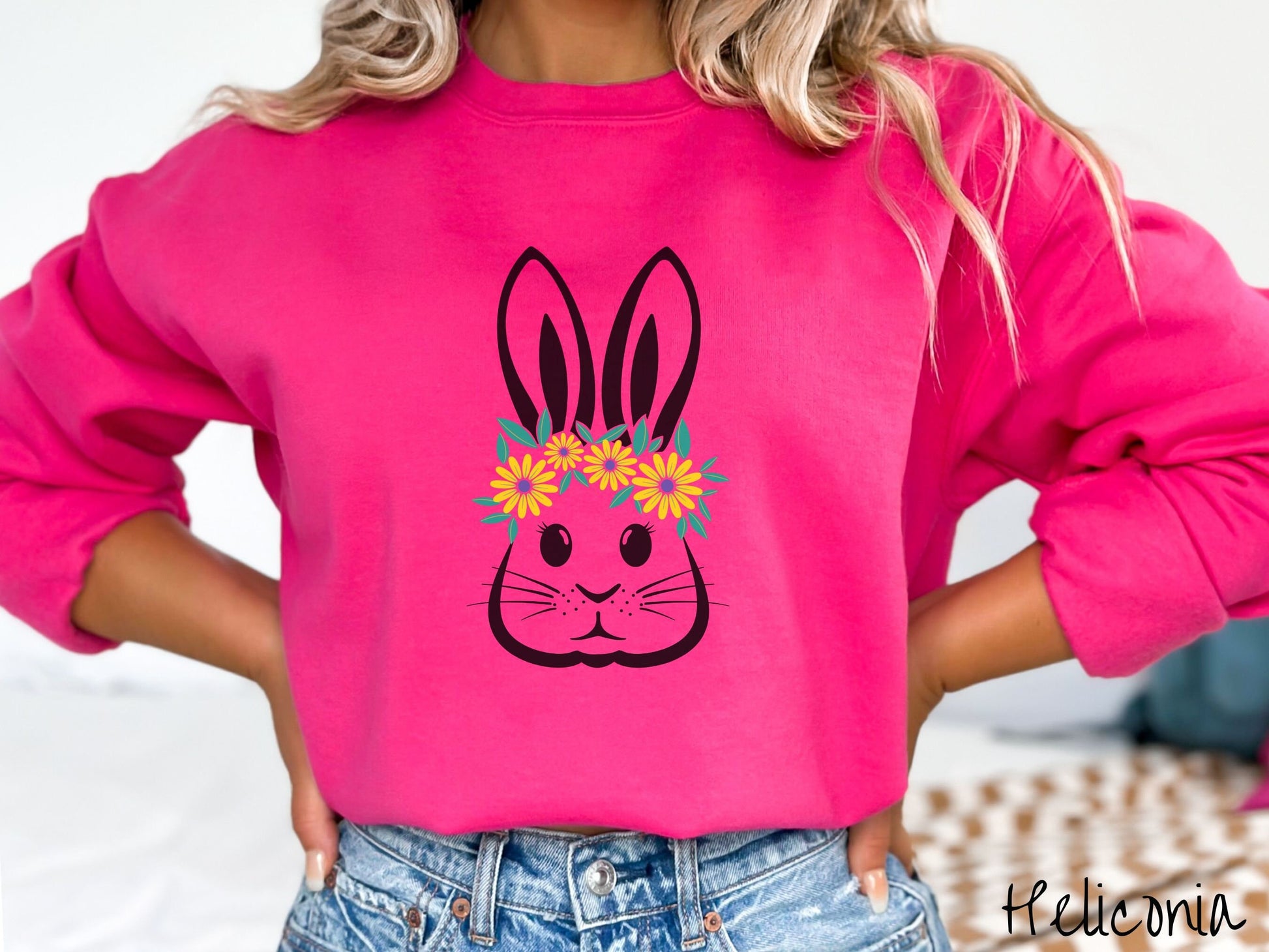 A woman wearing a cute, vintage heliconia colored sweatshirt with a black outline of a bunny rabbit with eyelashes and whiskers that has a yellow and purple flower headband resting below its large ears.
