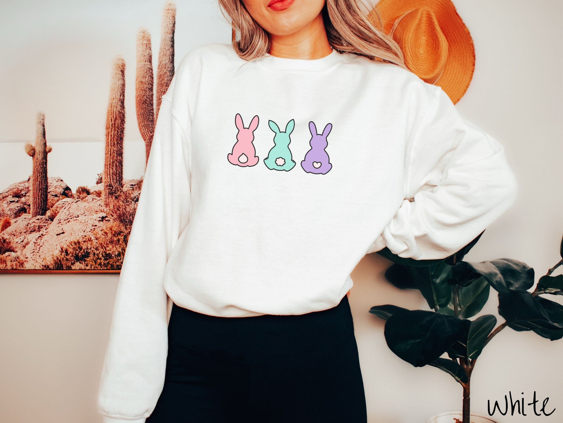 A woman wearing a cute, vintage white colored shirt with three colorful bunny rabbits sitting facing away. One is pink with a white tail, another bay with white tail, and the third is purple with a white, heart-shaped tail.
