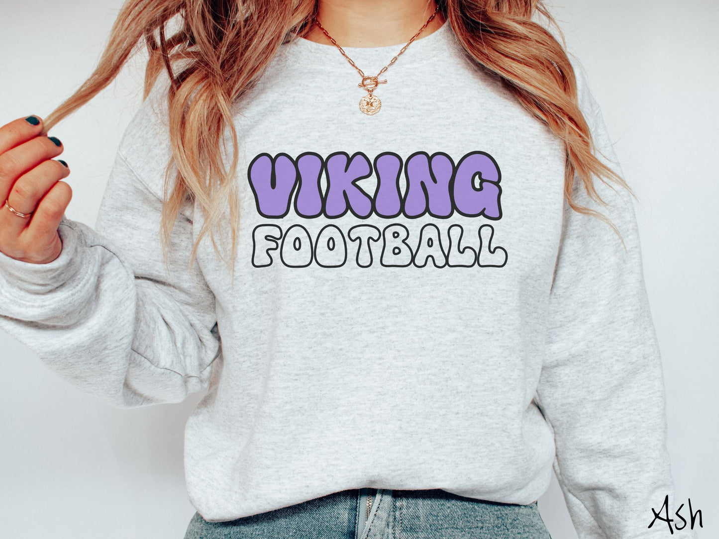 A woman wearing a cute, vintage ash colored sweatshirt with the word Viking across the front in purple, uppercase font. Below that is the word football in ash, uppercase font.