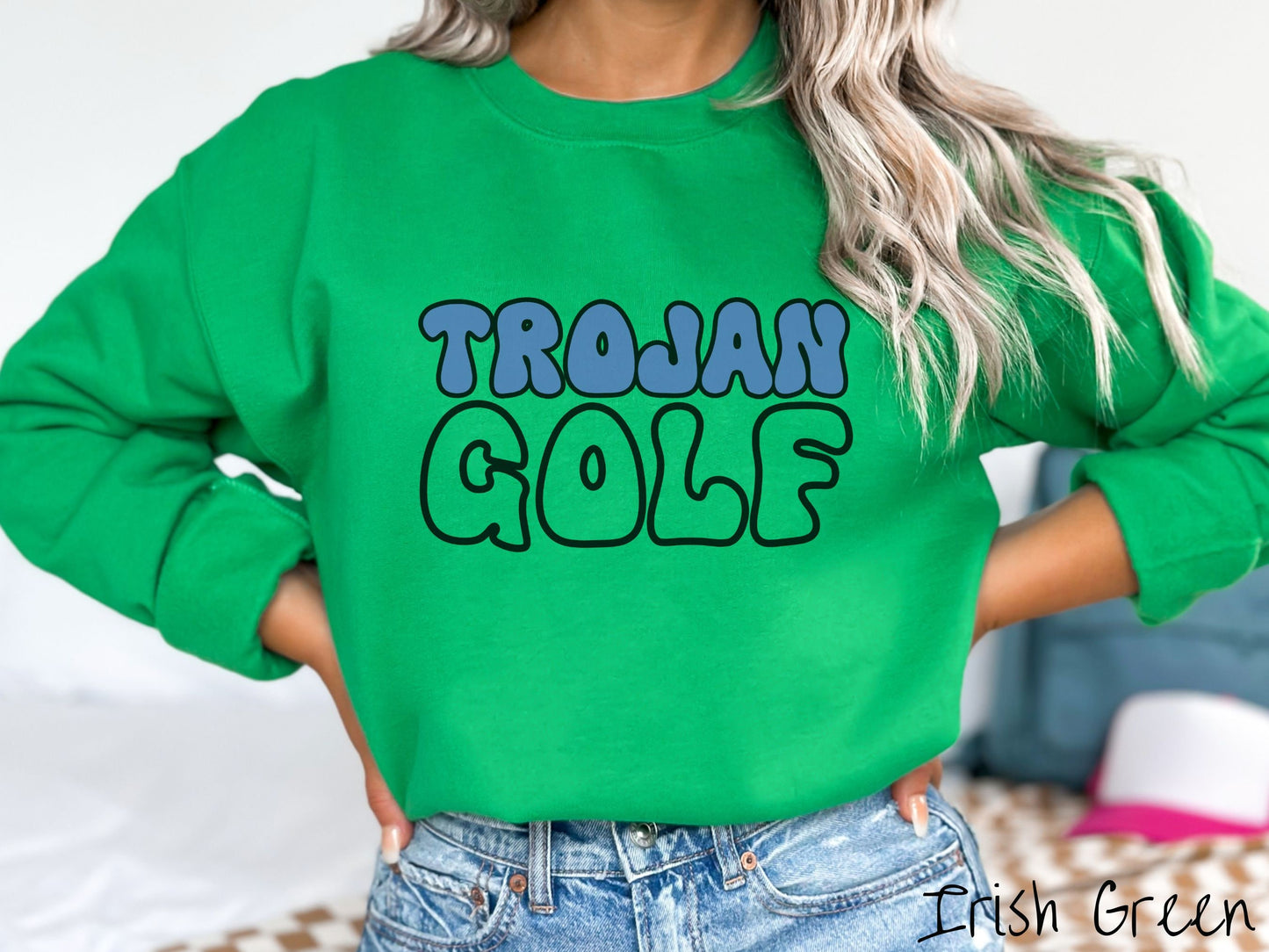 A woman wearing a cute, vintage Irish green colored sweatshirt with the word Trojan across the front in blue, uppercase font. Below that is the word golf in green, uppercase font.