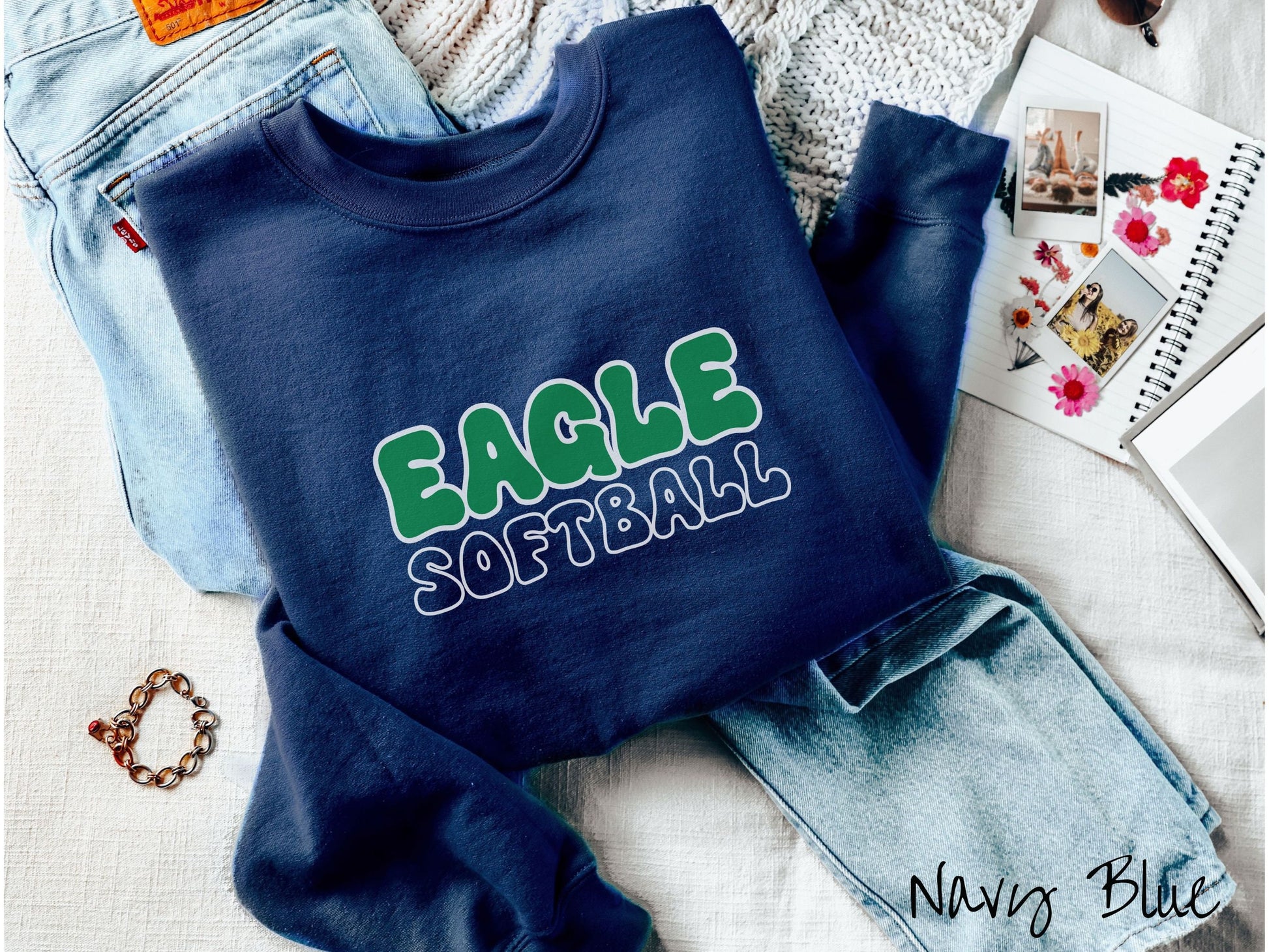 A cute, vintage navy blue colored sweatshirt with the word Eagle across the front in green, uppercase font. Below that is the word softball in blue, uppercase font.