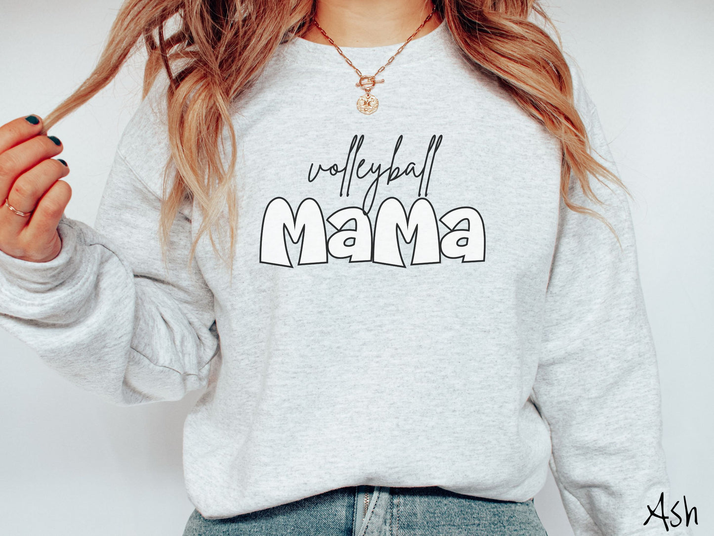 A woman wearing a cute, vintage ash colored sweatshirt with the word volleyball across the front in black, undercase cursive writing. Below that is the word Mama in large, white font.