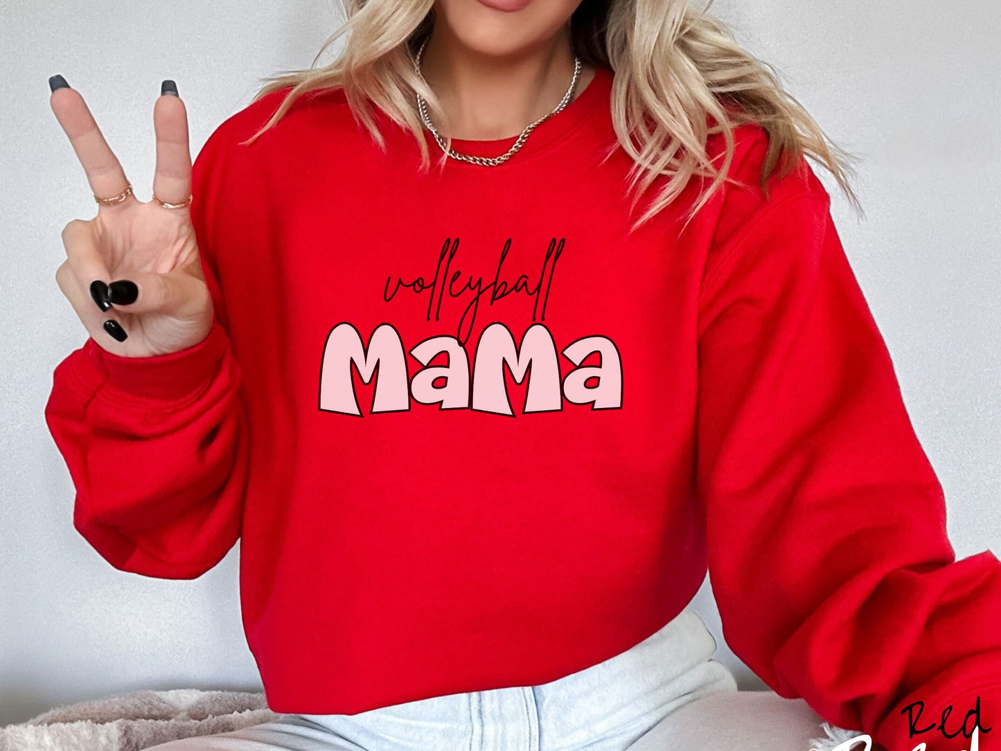 A woman wearing a cute, vintage red colored sweatshirt with the word volleyball across the front in black, undercase cursive writing. Below that is the word Mama in large, white font.