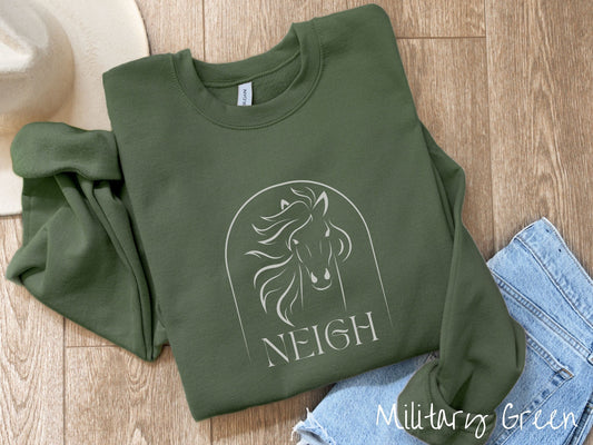 A woman wearing a cute, vintage military green colored comfy sweatshirt with a white silhouette outline of a horse facing forward, its hair blowing to the side. Below that is the word Neigh in white, cursive font.