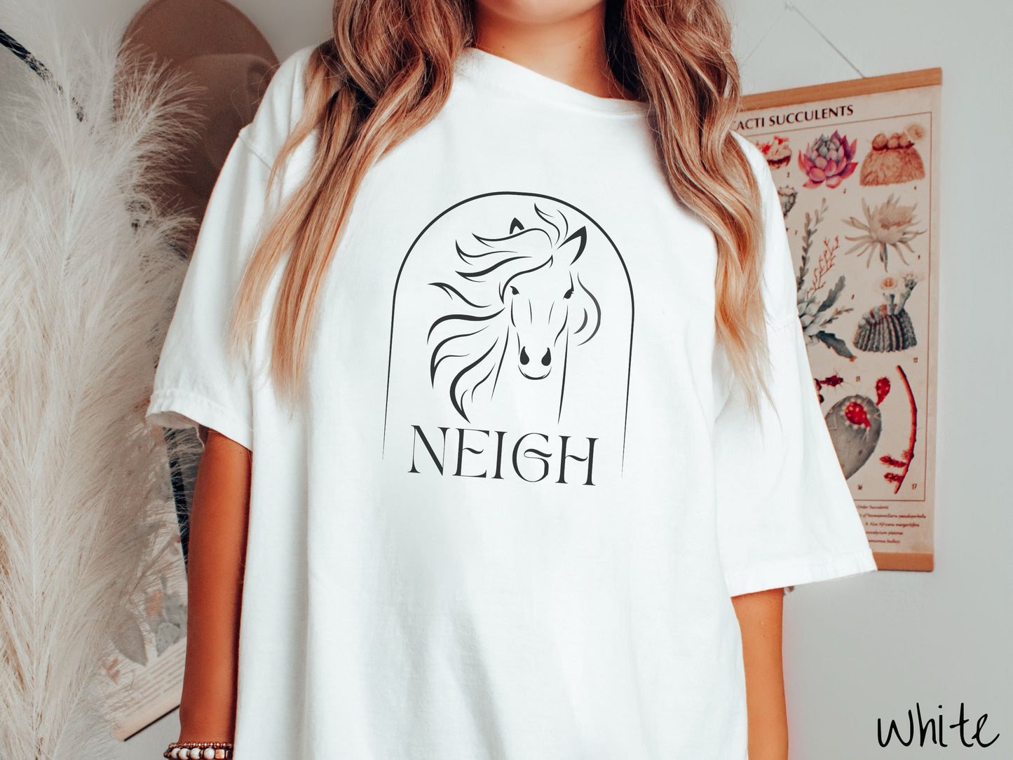 A woman wearing a cute, vintage white colored Comfort Colors shirt with a black silhouette outline of a horse facing forward, its hair blowing to the side. Below that is the word Neigh in black, cursive font.