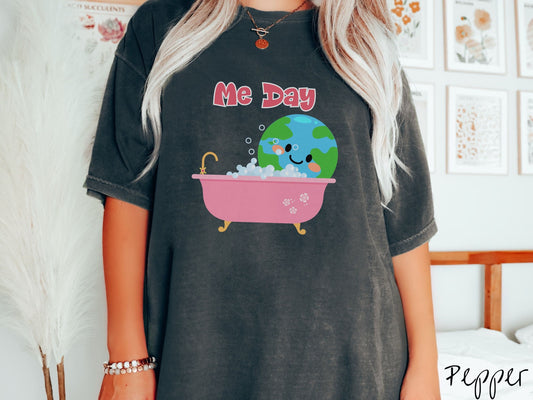 A woman wearing a cute, vintage pepper colored Comfort Colors shirt with the text Me Day in red font across the top. Below that is the Earth with a smiling face sitting in a pink bathtub enjoying a bubble bath.