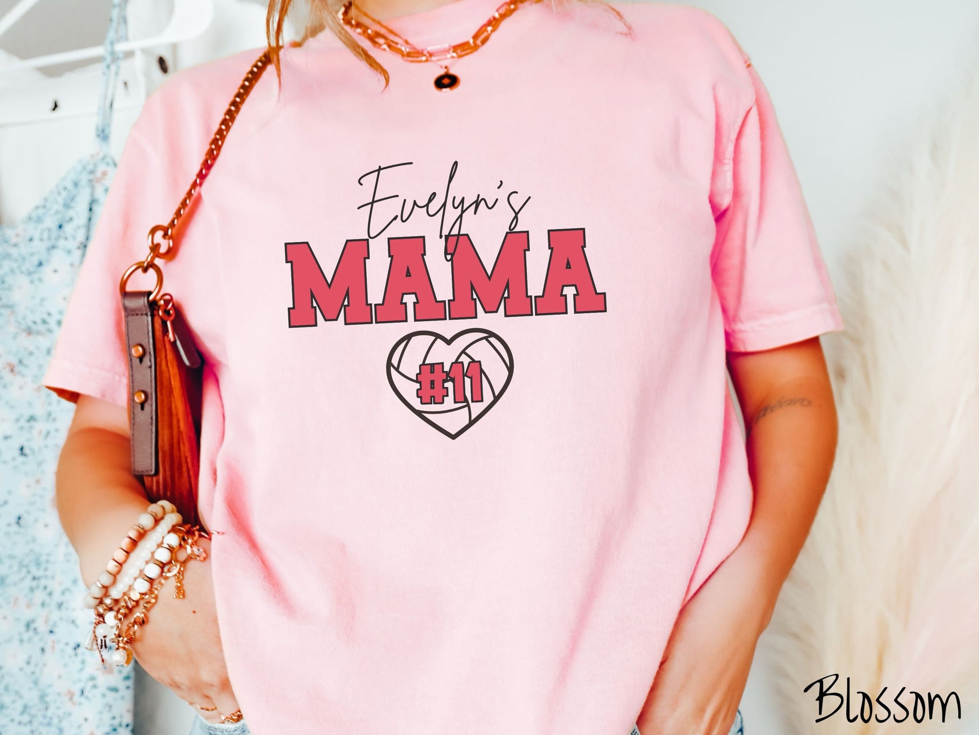 A woman wearing a cute blossom colored t-shirt with black and red text saying Evelyns Gran. Below is a black, heart-shaped volleyball outline with #11 in red font written across it.