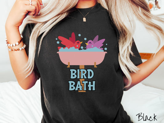 A woman wearing a cute, vintage black colored Comfort Colors shirt with a pink bathtub with a red bird and purple bird enjoying a bubble bath together. Below the bathtub are the words Bird Bath in light blue, uppercase font.