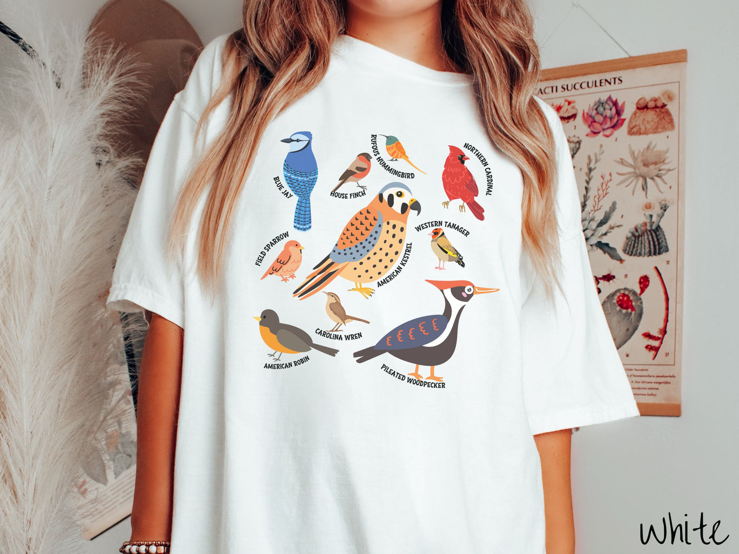 A woman wearing a cute, vintage white colored Comfort Colors shirt with pictures of nine different bird species and their names listed across the front. Some examples are the Blue Jay, House Finch, Western Tanager, and Carolina Wren.