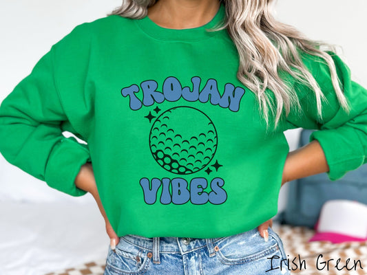 A woman wearing a cute Irish green colored sweatshirt with blue text saying Trojan Vibes. There is a golf ball outline with black twinkling stars around it between the text.