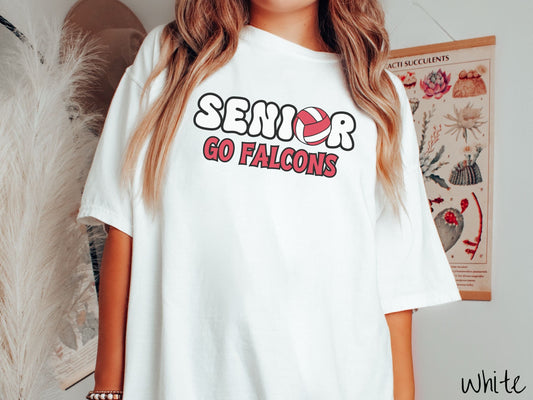 A woman wearing a cute white colored t-shirt with the word Senior in black and white font, the O in Senior is a red and white volleyball. Below Senior are the words in red and black font Go Falcons.