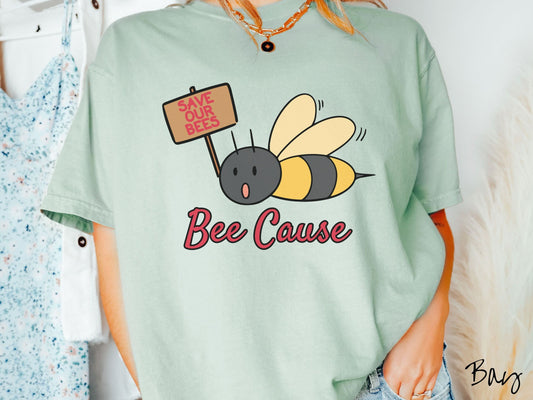 A woman wearing a cute, vintage bay colored comfy sweatshirt with the text Bee Cause in red, cursive font. Above that is a black and yellow honey bee speaking with its mouth open and holding a sign that reads Save Our Bees in red font.