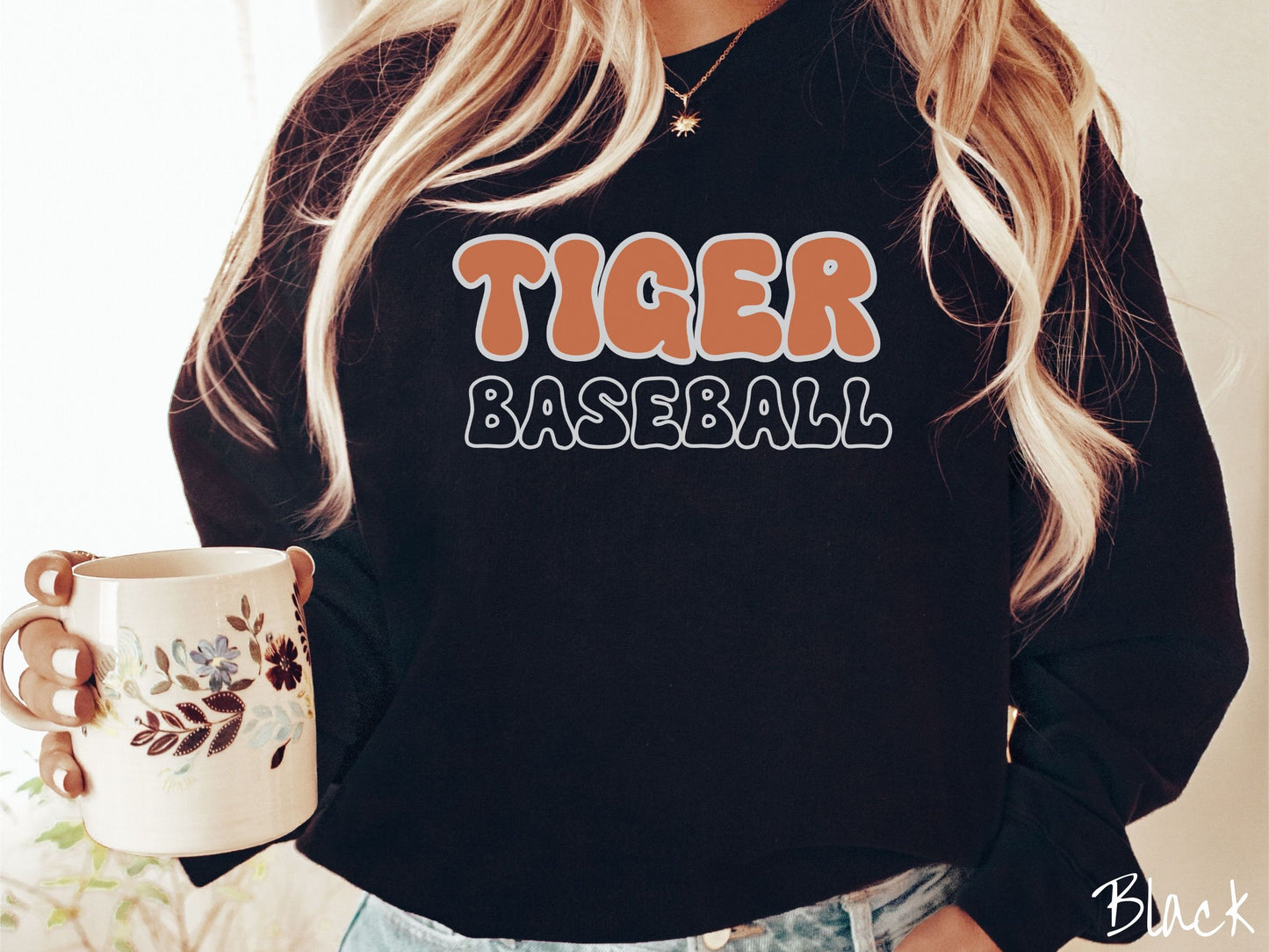 A woman wearing a cute, vintage black colored sweatshirt with the word Tiger across the front in orange, uppercase font. Below that is the word Baseball in black, uppercase font.