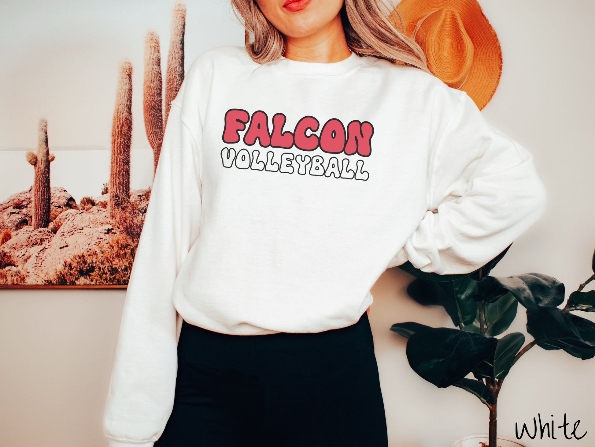 A woman wearing a cute, vintage white colored sweatshirt with the word Falcon across the front in red, uppercase font. Below that is the word volleyball in white, uppercase font.