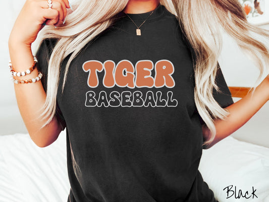 A woman wearing a cute, vintage black colored Comfort Colors shirt with the word Tiger across the front in orange, uppercase font. Below that is the word Baseball in black, uppercase font.