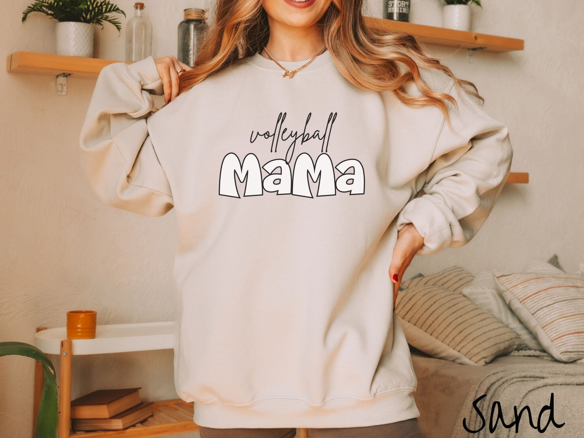A woman wearing a cute, vintage sand colored sweatshirt with the word volleyball across the front in black, undercase cursive writing. Below that is the word Mama in large, white font.