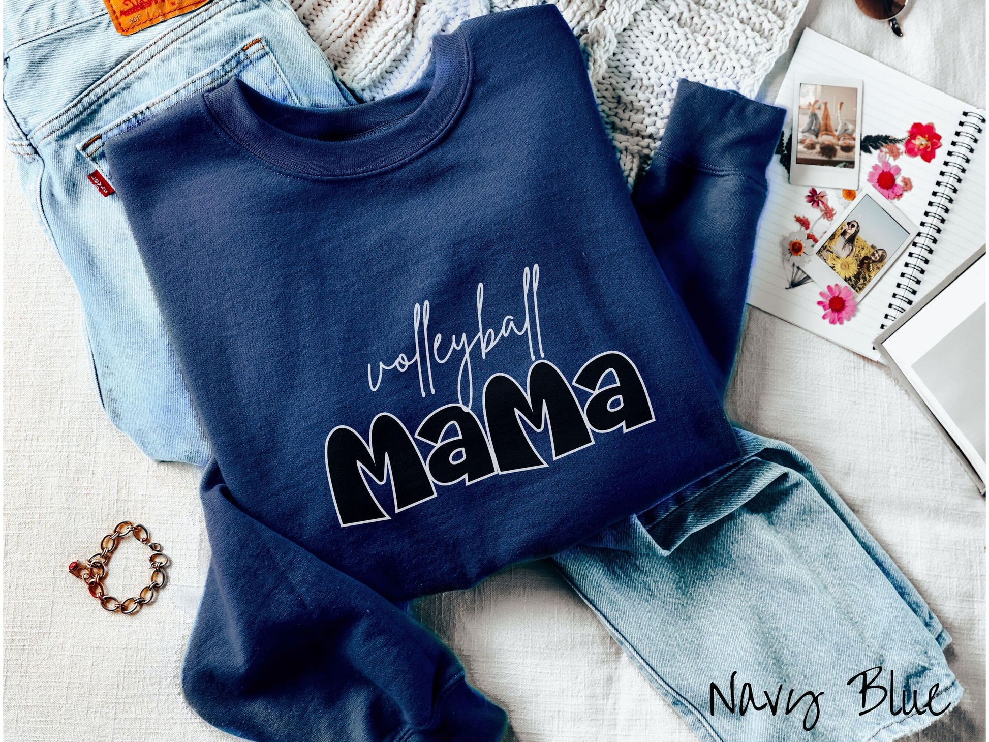 A woman wearing a cute, vintage navy blue colored sweatshirt with the word volleyball across the front in white, undercase cursive writing. Below that is the word Mama in large, black font.