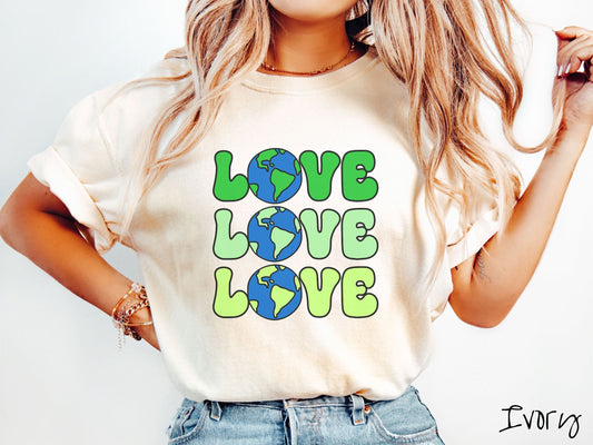 A woman wearing a cute, vintage ivory colored Comfort Colors shirt with the word Love listed vertically three times in varying shades of green, uppercase font. The Os in the words are pictures of the blue and green earth.