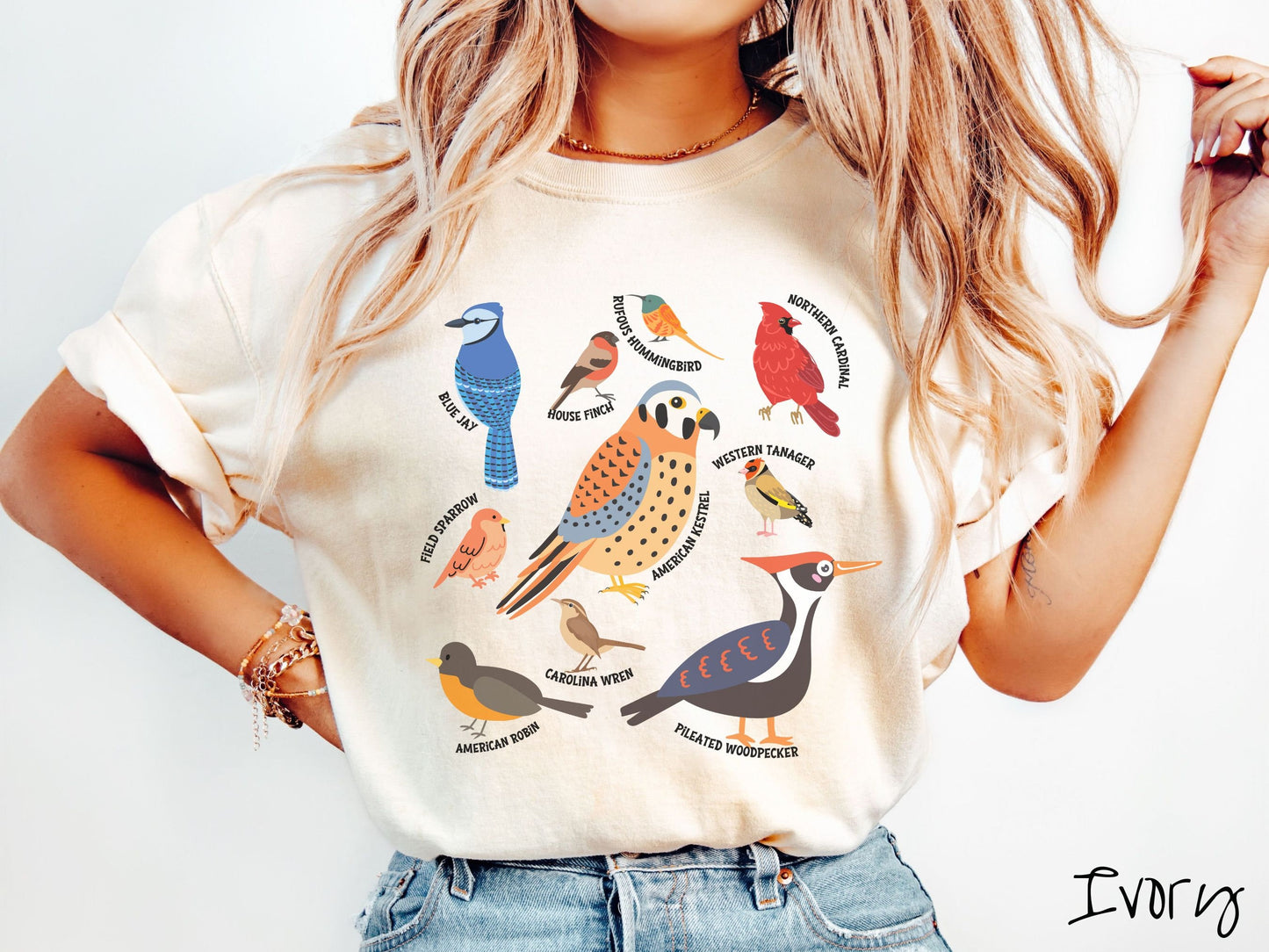 A woman wearing a cute, vintage ivory colored Comfort Colors shirt with pictures of nine different bird species and their names listed across the front. Some examples are the Blue Jay, House Finch, Western Tanager, and Carolina Wren.