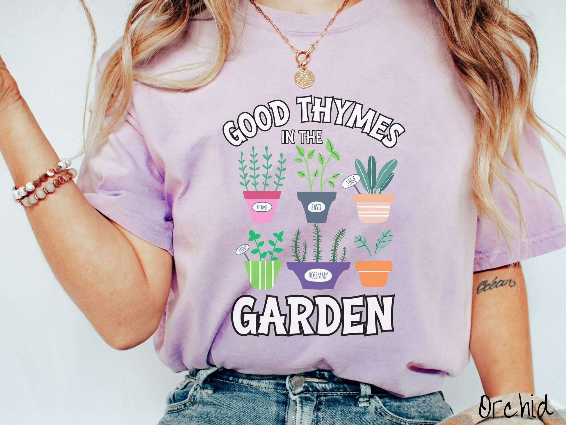 A woman wearing a cute, vintage orchid colored Comfort Colors t-shirt with the text Good Thymes in the Garden in white font. In between the text are different potted vegetables in colorful pots like thyme, basil, sage, and mint.