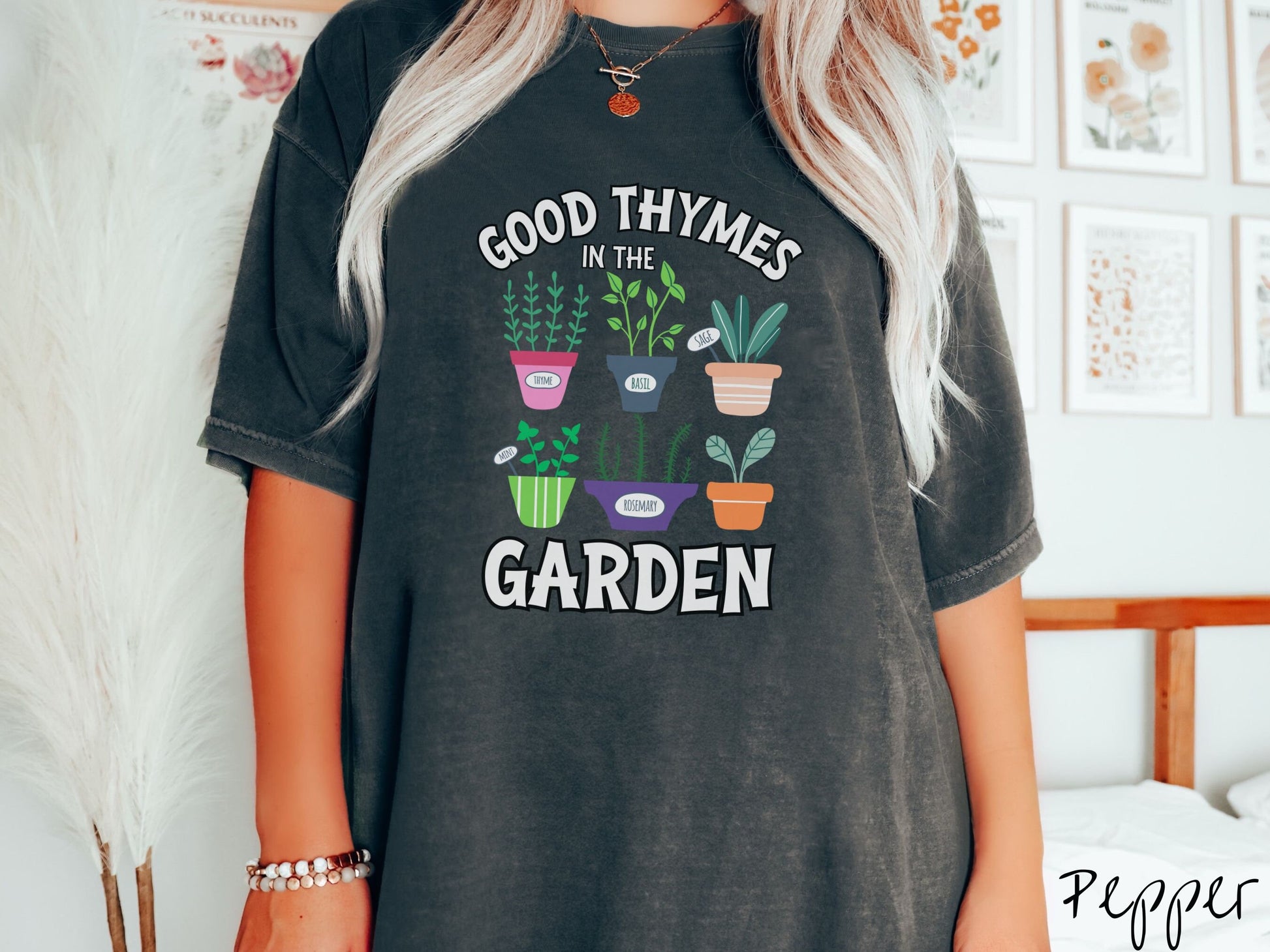 A woman wearing a cute, vintage pepper colored Comfort Colors t-shirt with the text Good Thymes in the Garden in white font. In between the text are different potted vegetables in colorful pots like thyme, basil, sage, and mint.
