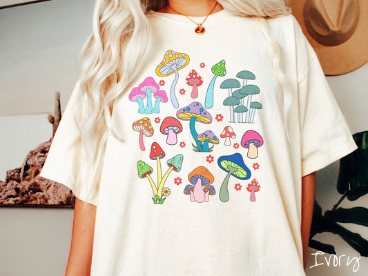 A woman wearing a cute, vintage ivory colored Comfort Colors t-shirt with many different colorful mushrooms displayed in a grid layout. Colors range from pink, yellow, red, green, blue, and orange.