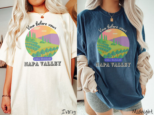 Two women wearing cute, vintage ivory and midnight colored Comfort Colors t-shirts with text Vino before vows and Katie’s Bachelorette Napa Valley, with a picture of a California wine vineyard with rows of trees in a meadow with purple mountains.