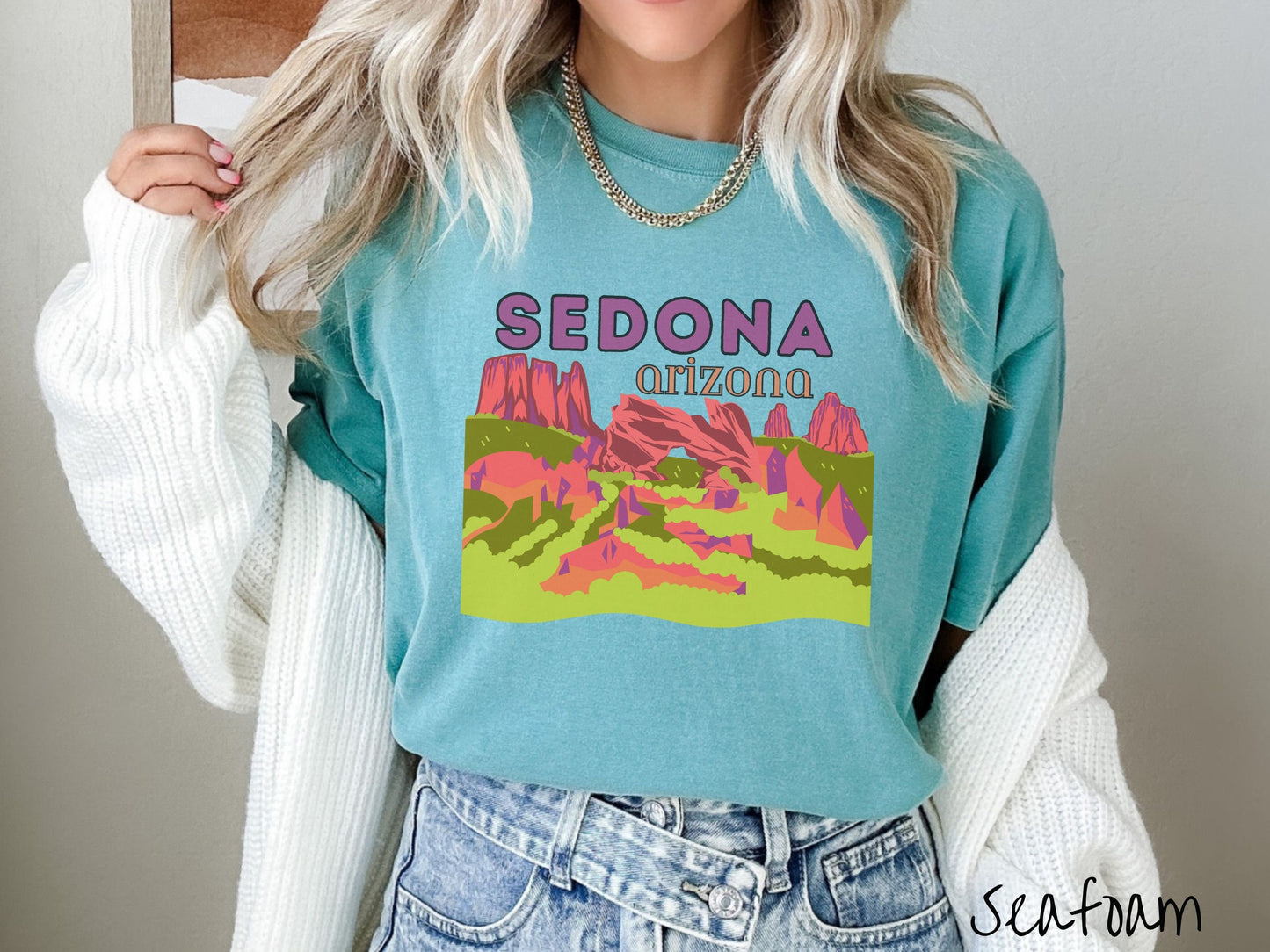 A woman wearing a vintage, seafoam colored comfort colors t-shirt with the text Sedona Arizona in purple and orange font, respectively, and below that is a picture of red rock canyons and green meadows.