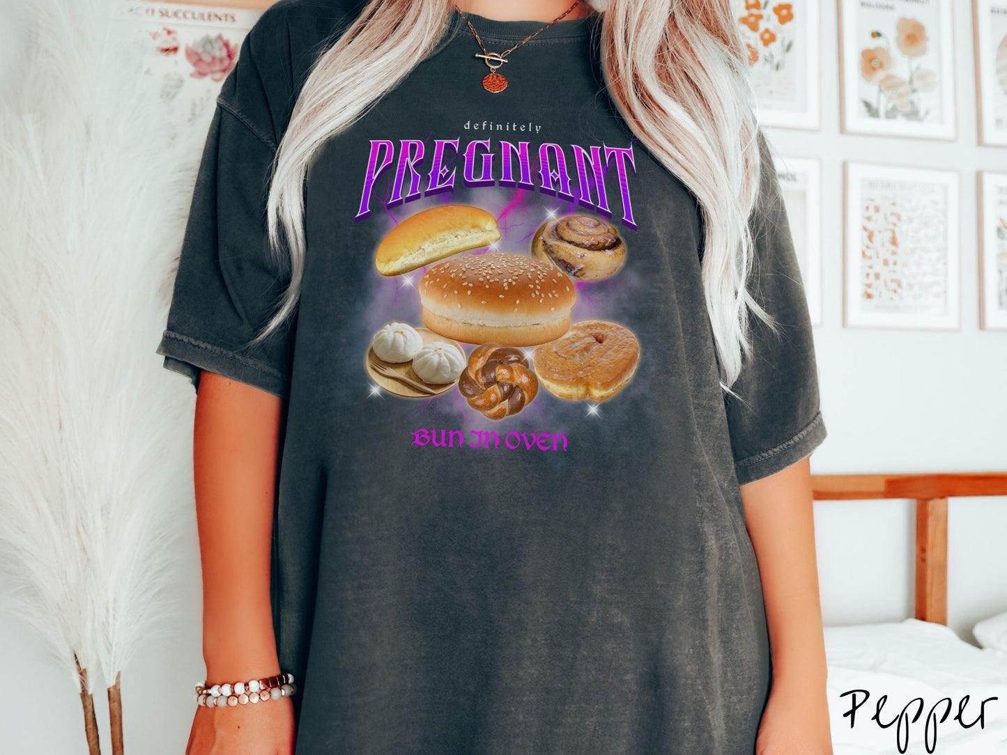 A woman wearing a vintage, pepper colored Comfort Colors t-shirt with the text Definitely Pregnant Bun In Oven in purple font. Between the text are different breads like hamburger and hotdog buns, cinnamon rolls, and donuts.