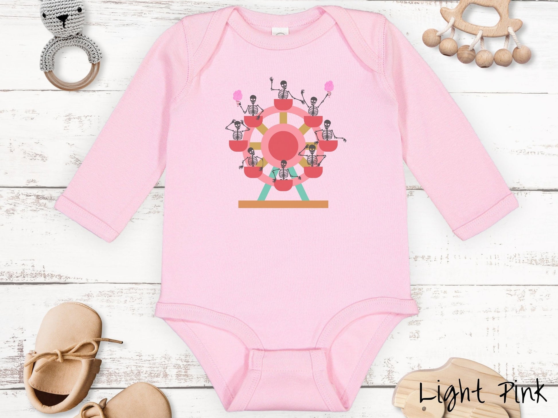 A cute light pink colored body suit with a ferris wheel filled with black skeletons waving and holding cotton candy as they go around the ride.