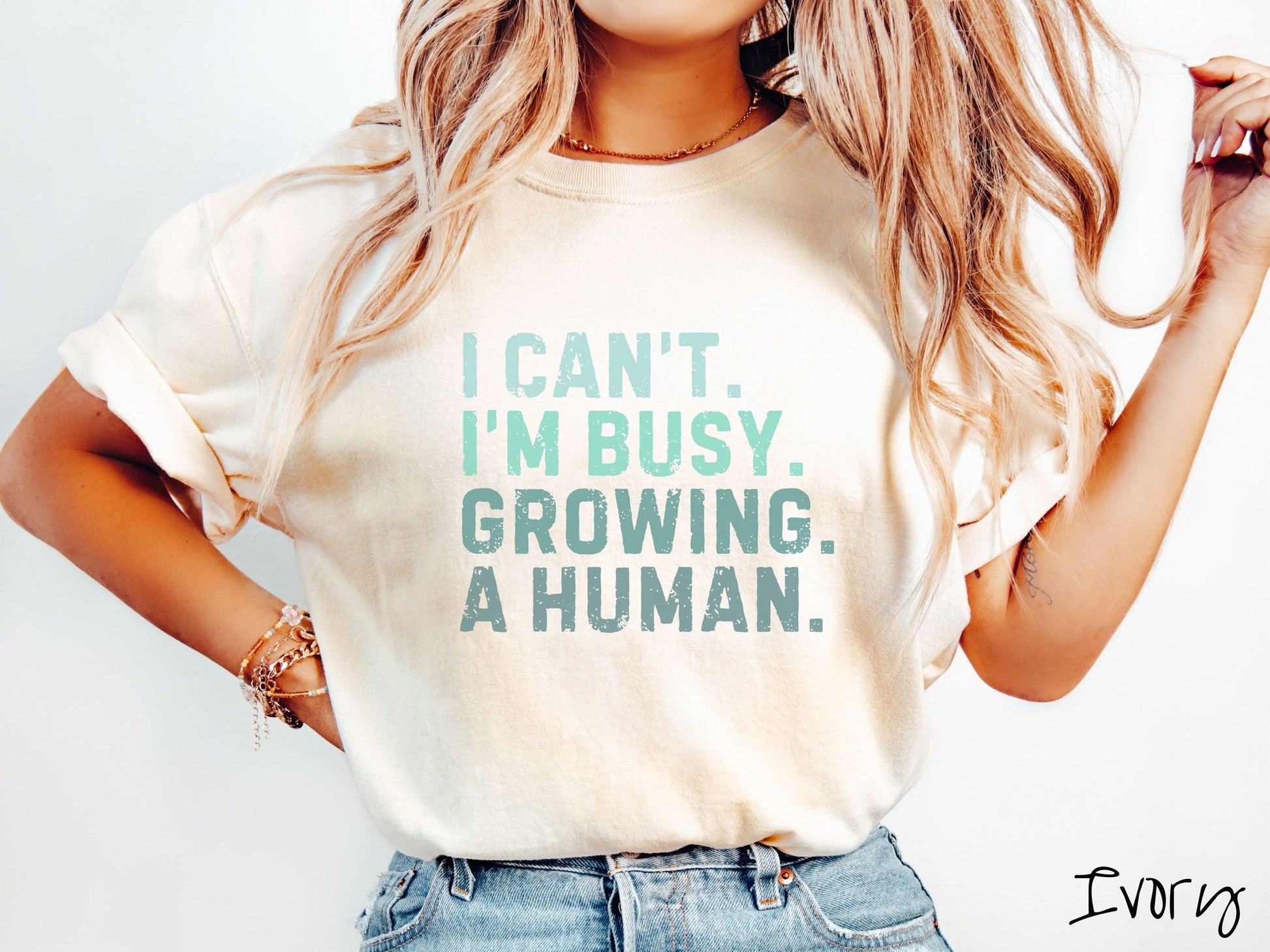 A woman wearing a vintage, ivory colored Comfort Colors t-shirt with the text listed vertically in varying shades of green font I Can’t. I’m busy. Growing. A human.