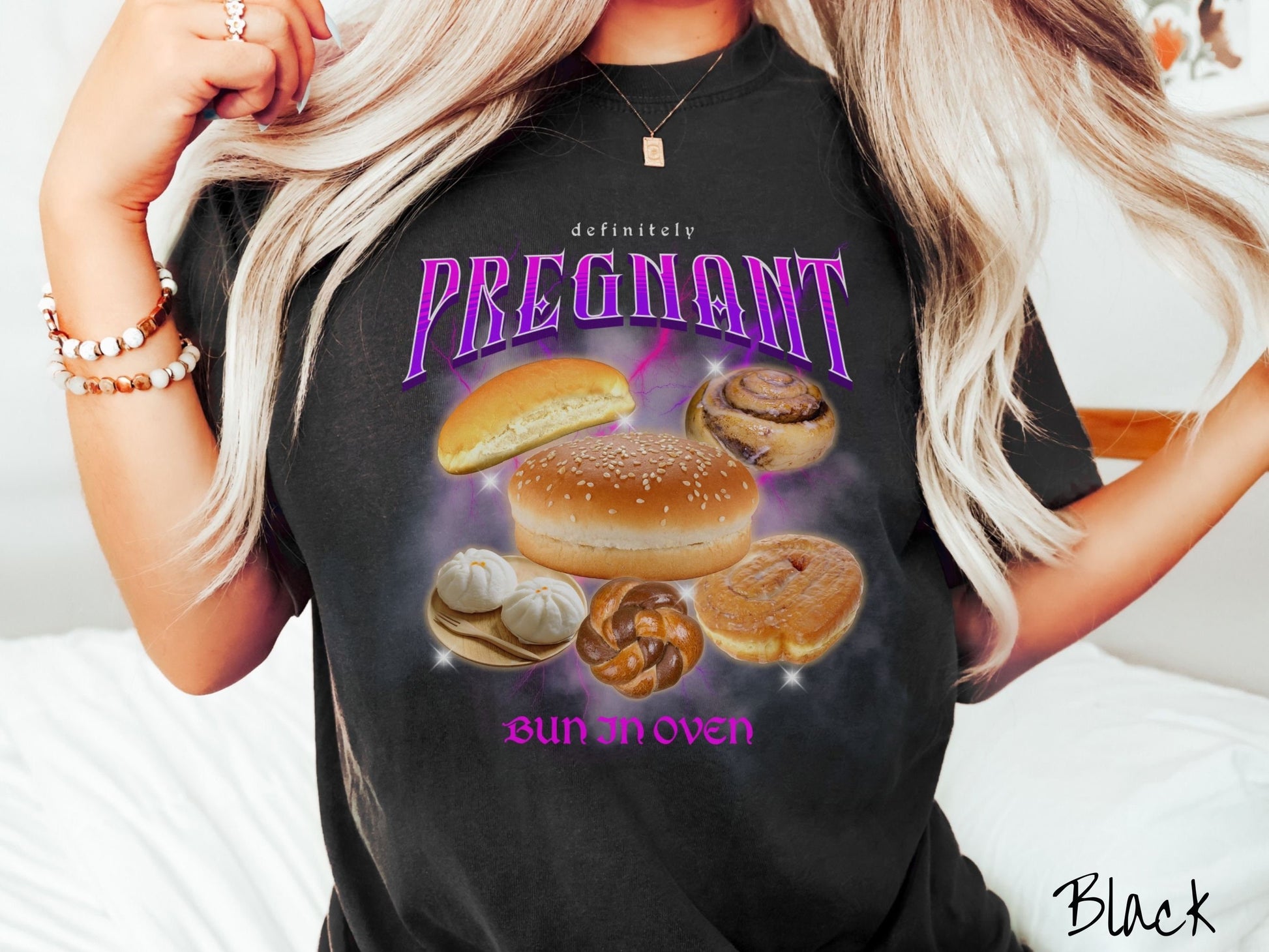 A woman wearing a vintage, black colored Comfort Colors t-shirt with the text Definitely Pregnant Bun In Oven in purple font. Between the text are different breads like hamburger and hotdog buns, cinnamon rolls, and donuts.